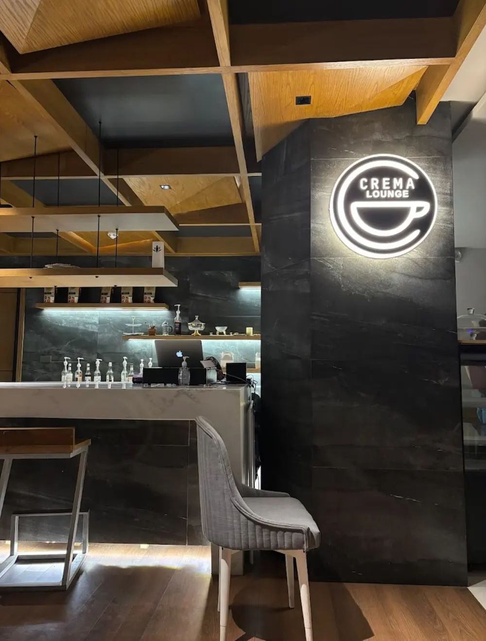 The lit Crema Lounge logo on a black marble wall beside the bar